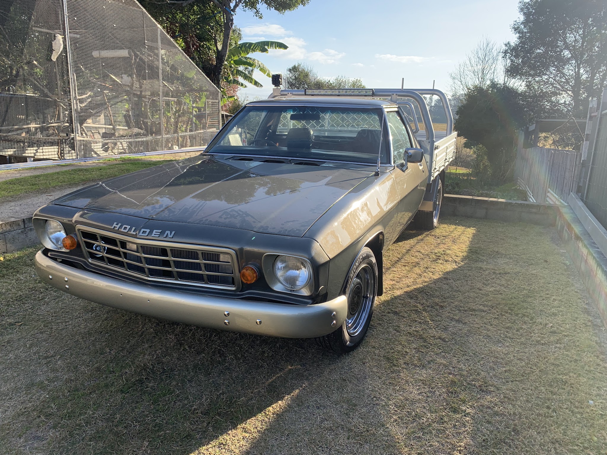 Grey Holden one tonner ute with a tray and light bar, parked on grass in late afternoon light