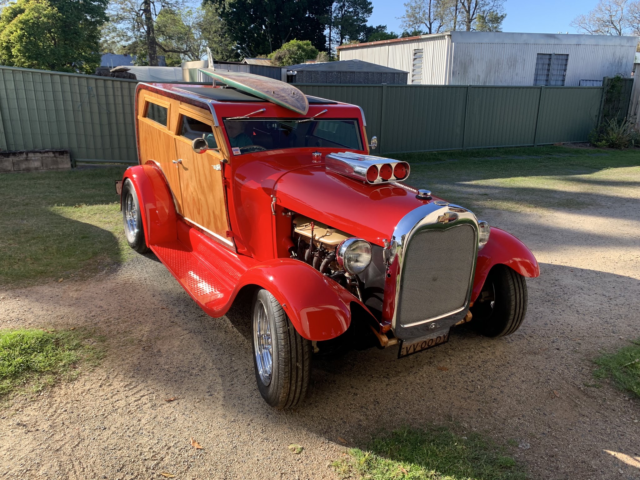 Red hot rod woody wagon with timber panels, a chromed injected motor through the bonnet and a wooden surfboard on the roof