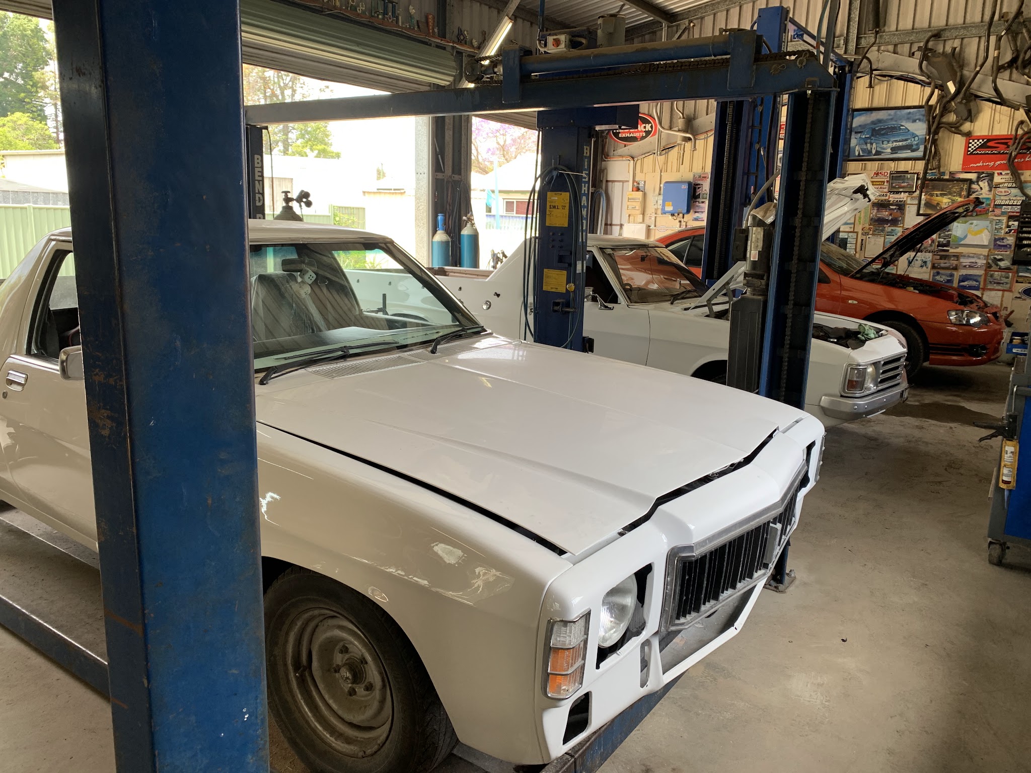 Inside the Wiblen Exhaust and Mechanical workshop in South Grafton, with a Holden ute in the foreground bay and a second car up on the hoist